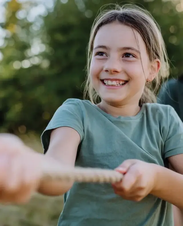 A smiling girl pulling a rope outdoors