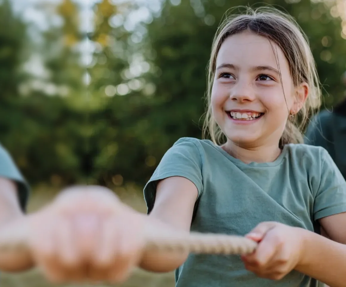 A smiling girl pulling a rope outdoors